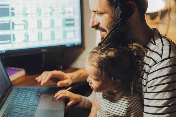 Stylish Bearded father working at home while babysitting his playful daughter