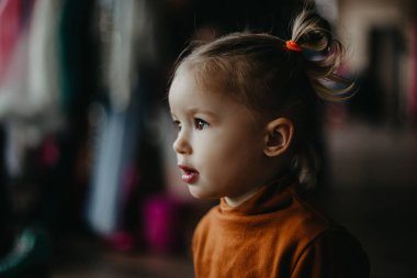 2 yaşındaki küçük çekici kız aynanın yanında makyaj yapan annesinin yanında oynuyor, bebek de annesinin aynanın önünde poz vermesini izliyor.