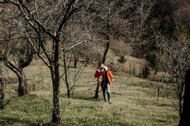 Bahar bahçesinde genç bir adam ev şöminesi için odun topluyor ve kesiyor.