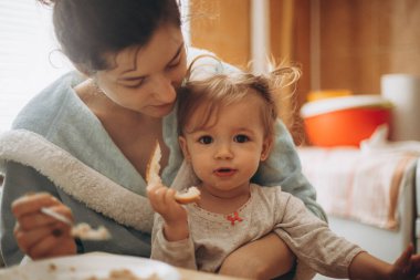 seçici odak, gürültü efekti: kirli yüzlü küçük bir kız annesiyle küçük bir mutfakta kahvaltı yapıyor.