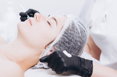 Profesyonel kozmetik uzmanının elleri kaplıca salonunda müşterinin yüzüne maske takar. Kozmetik dolabınızın veya kaplıcanızın reklamını yapmak için ideal bir ortam.