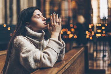 Din, inanç, ahenk ve halk konsepti: Kilise cemaati üyesi dua etmek ve gönülden dua etmek için elleri bağlı bir bankta oturur. Boşluğu kopyala