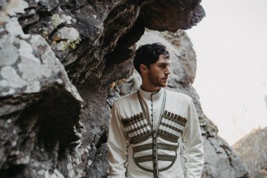 Gürültü efekti, seçici odak: Beyaz milli takım elbise giymiş şık bir Gürcü. Kafkasya dağlarında düğün sırasında Gürcü damadın portresi