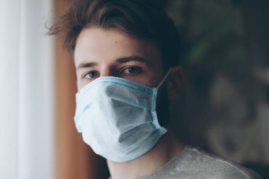Coronavirus karantinasında koruyucu maske takmış bir adam camdan dışarı bakıyor.