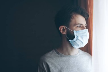 Coronavirus karantinasında koruyucu maske takmış bir adam camdan dışarı bakıyor.