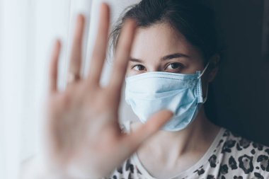 Kadın el işaretini gösteriyor, virüs ve enfeksiyonlara karşı korunmak için maske takmış bir kız.