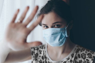 Kadın el işaretini gösteriyor, virüs ve enfeksiyonlara karşı korunmak için maske takmış bir kız.