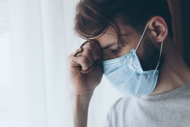 Tıbbi maske takan bir gencin portresi evde ya da pencerenin karşısındaki hastane koğuşunda karantinaya alınmış.