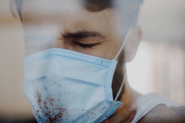 Koruyucu bir maske takan genç bir adamın portresi ve evde karantina. Gönüllü olarak kendini izole eden hastalar ve koronavirüs belirtileri.
