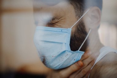 Coronavirüs salgını sırasında maskeli bir adamın portresi. Tehlikeli bir viral hastalığın belirtileri: Boğaz ağrısı, öksürük, ateş.