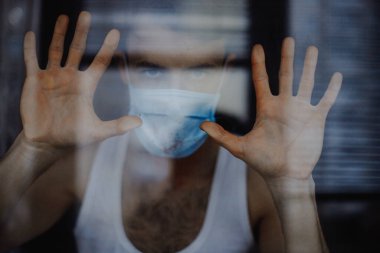 Koruyucu bir maske takan genç bir adamın portresi ve evde karantina. Gönüllü olarak kendini izole eden hastalar ve koronavirüs belirtileri.