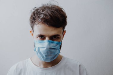 Koruyucu bir maske takan genç bir adamın portresi ve evde karantina. Gönüllü olarak kendini izole eden hastalar ve koronavirüs belirtileri.