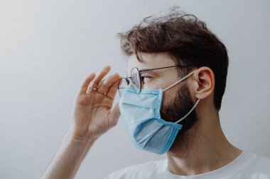 Koruyucu bir maske takan genç bir adamın portresi ve evde karantina. Gönüllü olarak kendini izole eden hastalar ve koronavirüs belirtileri.
