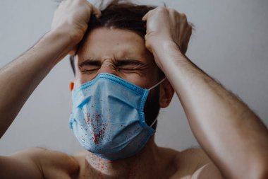 Hastalıklı, koruyucu bir maske takan genç bir adam. Kan sıçramış. Bu da hastanın sağlığının bozulduğunu gösteriyor.