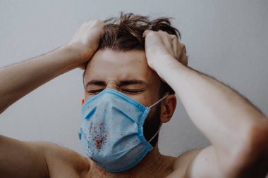 Hastalıklı, koruyucu bir maske takan genç bir adam. Kan sıçramış. Bu da hastanın sağlığının bozulduğunu gösteriyor.