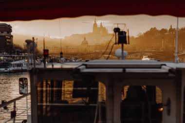 14.02.2020 Prag, Çek Cumhuriyeti: Charles Köprüsü 'nün altındaki Vltava Nehri' nde gün batımında antik bir kilisenin bulunduğu tepeye bakan bir turist teknesinin üst güvertesinden manzara