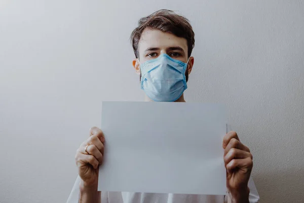Ένας Άνδρας Που Φοράει Ιατρική Μάσκα Κρατά Ένα Λευκό Φύλλο — Φωτογραφία Αρχείου