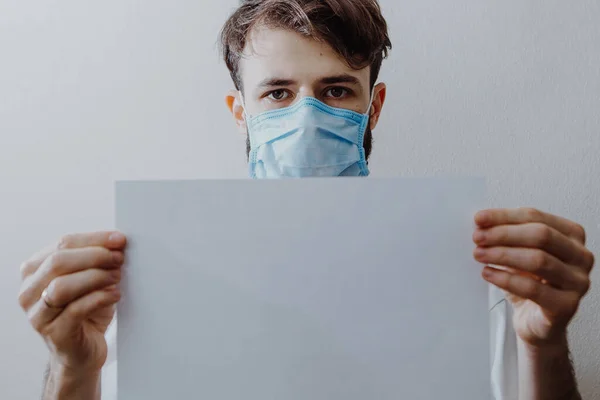 Tıbbi Maske Takan Bir Adam Beyaz Bir Kağıdı Tutuyor — Stok fotoğraf