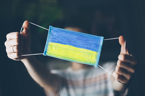 medical mask in hands of man, with the flag of   Ukraine painted. Copy space