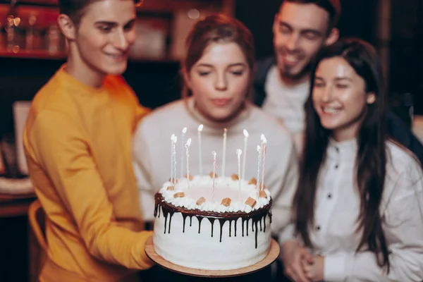 attractive girl blows out the candles on the cake and makes a wish near the best friends who came to congratulate her on her birthday