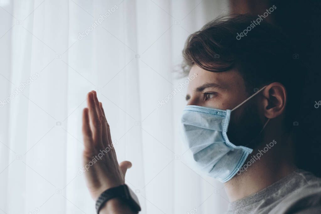 Pandemic. Sick man of corona virus looking through the window and wearing mask protection and recovery from the illness in home.