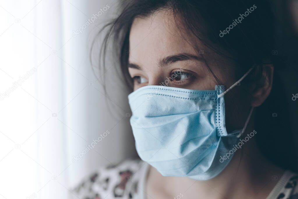 portrait of a girl wearing a protective medical mask. A woman who looks out the window during quarantine isolation