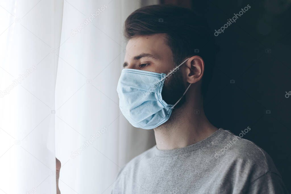 sick young man wearing protective medical mask standing in front of window in hospital ward
