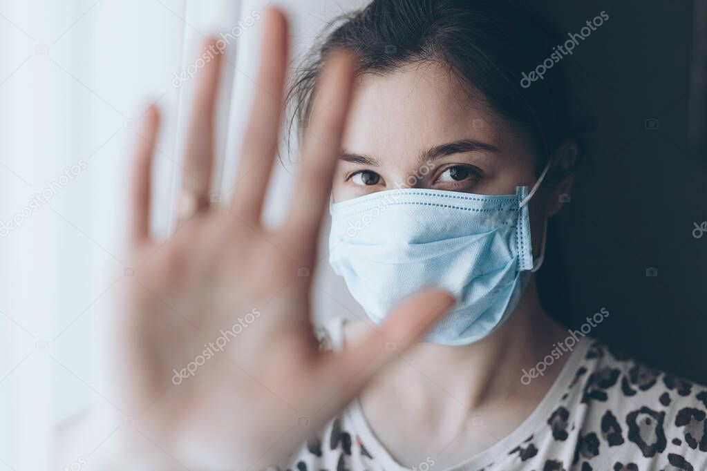 Woman shows hand stop sign, girl dressed in mask for protection against viruses and infections