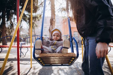 Anne ve bebeğin çocuk parkında sonbahar yürüyüşü. Tatlı bir çocuk salıncakta sallanıyor, lunapark treninden iniyor, gülüyor ve seviniyor..