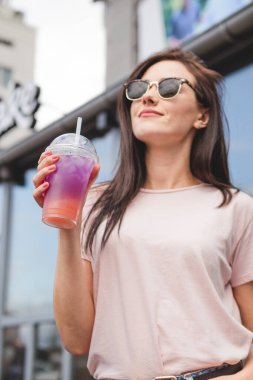 Güzel ve çekici bir kadın elinde plastik bardakla çok renkli soğuk bir yaz kokteyli tutuyor. Gülümsemesi ve neşeli bir havası var.