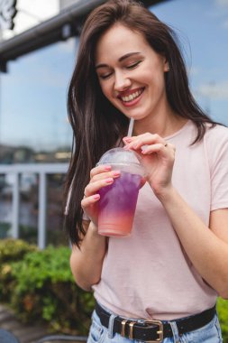 Güzel ve çekici bir kadın elinde plastik bardakla çok renkli soğuk bir yaz kokteyli tutuyor. Gülümsemesi ve neşeli bir havası var.