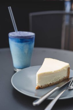 Klasik tariflere göre hazırlanmış bir dilim peynirli kek: kurabiye, tereyağı, krema ve süzme peynirden yapılmış. Tabaktaki cheesecake, bir fotoğrafın diğer detaylarıyla uyumlu renk kombinasyonunda.