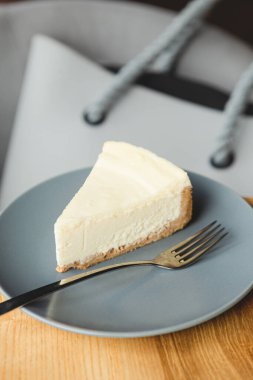 Klasik tariflere göre hazırlanmış bir dilim peynirli kek: kurabiye, tereyağı, krema ve süzme peynirden yapılmış. Tabaktaki cheesecake, bir fotoğrafın diğer detaylarıyla uyumlu renk kombinasyonunda.