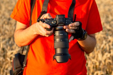 01.08.2019 Kyiv, Ukrayna: Akşam güneşinde bir tarlada çekim yaparken elinde kamera tutan bir adamın fotoğrafı,