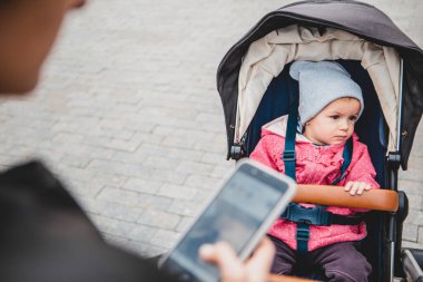 Bebek arabasındaki bebek, annem tarafından yürüyüşe çıkarıldı. Bebek üzgün çünkü annem ona dikkat etmiyor ve sürekli telefona bakıyor.