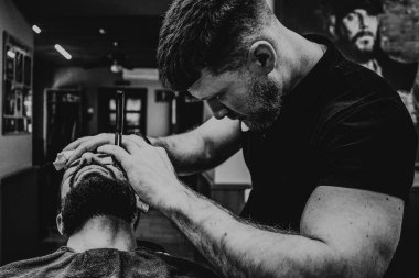 Forma giriyorum. Yakından bakınca, sakallı, sakallı, kaslı kuaför ya da berber tarafından tıraş edilen genç, şık sakallı bir adam görülüyor. Seçici odak noktası, gürültü etkisi.