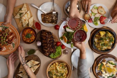 Dostça bir yemek. Kırsal ahşap masada bir sürü lezzetli ve tatmin edici yemekle birlikte yemek yiyen bir grup insanın üst düzey görüntüsü.