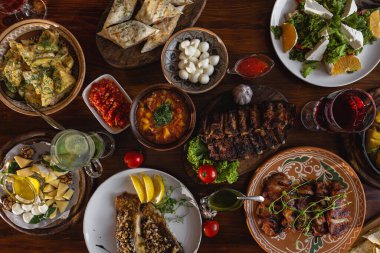 Çeşitli yiyeceklerle dolu yemek masası, tavada sebzeli kızarmış et, salata ve atıştırmalıklar, üst manzara.