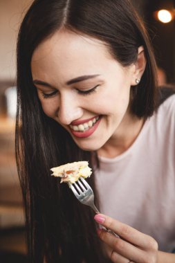 Enfes bir gülümsemesi ve güzel gözleri olan bir kadın, samimi bir kafede arkadaşıyla kahvaltı yapıyor. Çatal yer, kek yer ve masada bir sandalyede oturup çay içer.