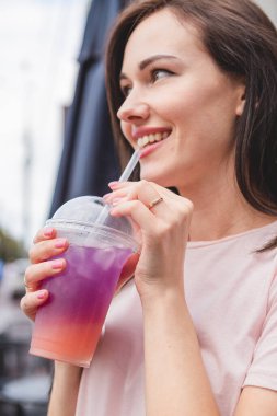 Güzel ve çekici bir kadın elinde plastik bardakla çok renkli soğuk bir yaz kokteyli tutuyor. Gülümsemesi ve neşeli bir havası var.