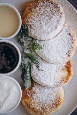 Lezzetli ve doyurucu bir tatlı, ev yapımı süzme peynir tavada kızartılmış ve sosla servis edilmiş. Cheesecake, taze reçel ve nane. Süzme peynirli krep ya da kremalı börek. Tabakta pudra şekeri. 
