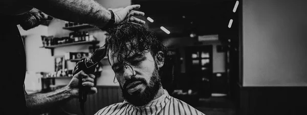 Close-up of a young hipster guy in a barbershop hairdresser cutting hair with scissors and a typewriter, blow-drying. Concept men\'s place, toned photo. Soft focus, copy space