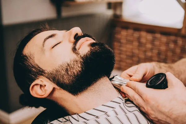 Confident man visiting hairstylist in barber shop. Beard styling and cut. Close up cropped photo of a styling of a brunette beard. Trendy and stylish. barber shop concept.Selective focus, noise effect