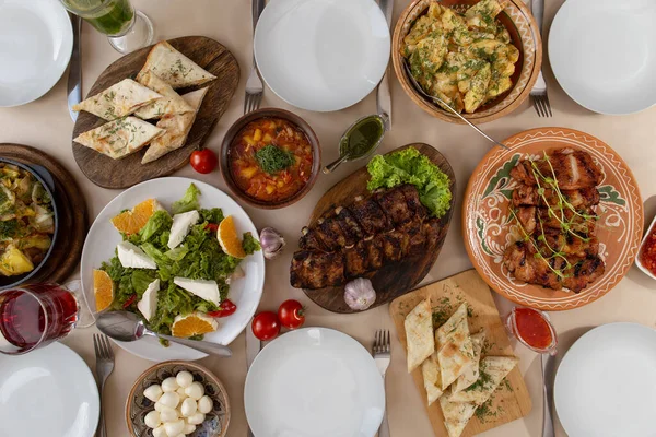 Dinner table with variety food, fried meat with vegetables in a pan, salad and snacks, top view