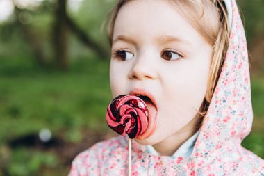 3 yaşındaki küçük bir kız yağmurlu bir yaz gününde parkta yürürken renkli bir girdap şekeri yalıyor.