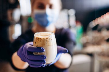 Barista karantina sırasında koruyucu maske ve lastik eldiven takarak kahve servisi yapıyor.