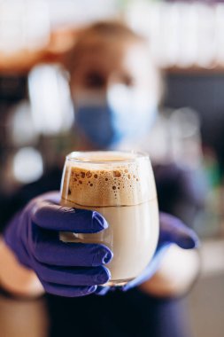 Barista karantina sırasında koruyucu maske ve lastik eldiven takarak kahve servisi yapıyor.