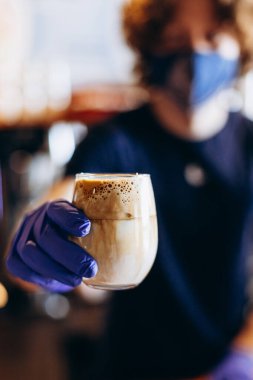Barista karantina sırasında koruyucu maske ve lastik eldiven takarak kahve servisi yapıyor.