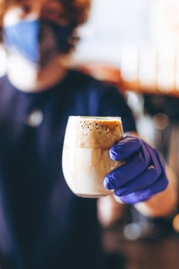 Barista karantina sırasında koruyucu maske ve lastik eldiven takarak kahve servisi yapıyor.