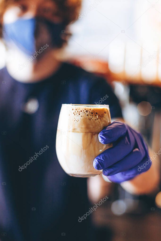 Barista serves a cup of coffee during quarantine wearing a protective mask and rubber gloves